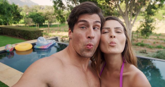 Selfie of happy caucasian couple making silly faces by swimming pool in sunny garden. Summer, fun, communication, vacations, free time, relaxation, relationship, togetherness and lifestyle, unaltered.