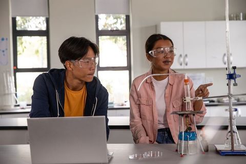Asian students conducting chemistry experiment with laptop and test tube in modern school lab