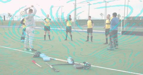 Field hockey coach leading team warm-up on artificial turf, players wearing yellow jerseys