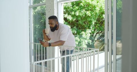 Man Relaxing on Balcony Using Smartphone and Drinking Coffee