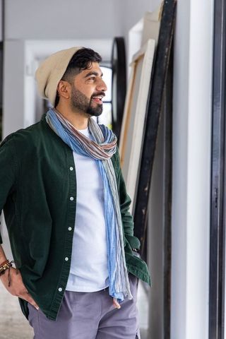 30s creative man standing by window in loft studio wearing beanie and striped scarf