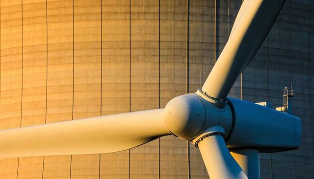 Sunlit wind turbine hub and blades showing bolted seams against concrete tower