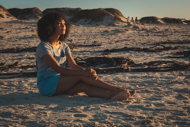 African american woman sitting on beach and relaxing during sunset. summer beach vacation by the sea.