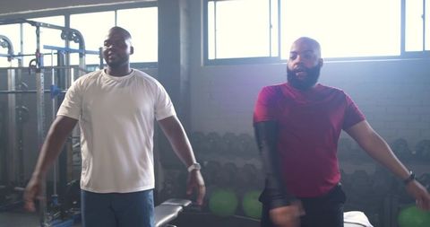 Sunlit african american men training together near dumbbell rack in gym fitness session