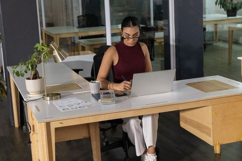 Focused professional woman typing on laptop in modern minimalist office workspace