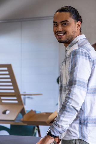 Smiling asian man standing at modern coworking desk with laptop stand and open box