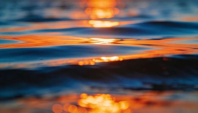 Rippling ocean surface reflecting golden sunset light with teal troughs and bokeh