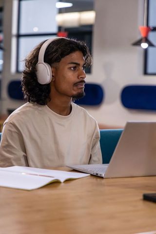 Indian man studying with laptop and white headphones in modern coworking space