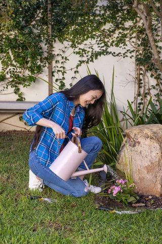 Young Woman Enjoying Gardening While Watering Flowers in Sunny Backyard