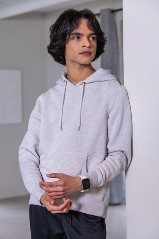 Contemplative asian teen leaning on wall wearing grey hoodie and smartwatch minimal interior