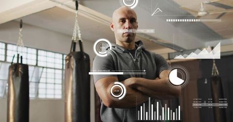 Posing muscular trainer wearing gray hoodie in boxing gym with hud performance overlays