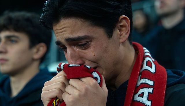 Crying young football fan clutching team scarf in stadium showing raw emotion