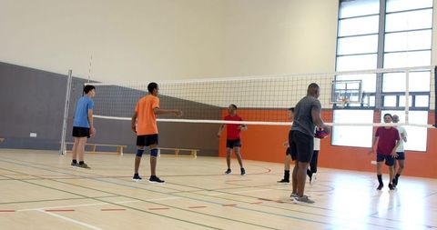 Diverse male team playing volleyball indoors on gym court showing teamwork and fitness