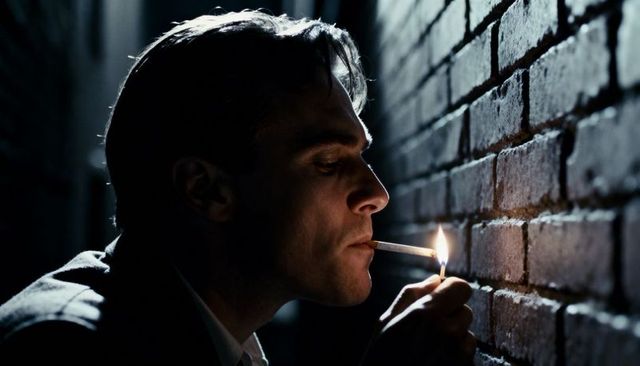 Nocturnal noir: man lighting cigarette by brick wall in alley, moody silhouette