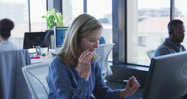 Customer service representative assisting a customer while working in a modern office with large windows. Ideal for illustrating concepts related to customer support, communication services, and corporate work environments.