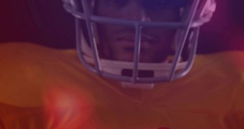 Football player facing camera wearing helmet and gold jersey with cinematic rim lighting
