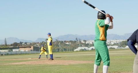 Batter preparing to swing while pitcher delivering pitch on sunny community baseball field