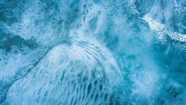 Aerial abstract ribbed ice floe drifting over polar lagoon showing melt channels and foam