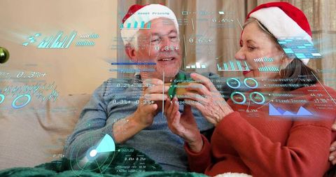 Senior couple wearing santa hats using smartphone with ar financial charts at home