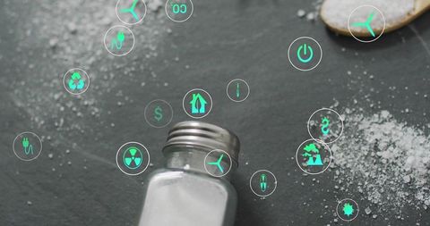 Spilled glass salt shaker on dark slate with neon green sustainability and energy icons