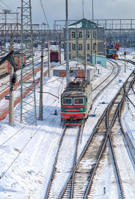 Freight train moving along snow-covered railway tracks in a winter setting. Ideal for illustrating winter transportation, railway logistics, seasonal travel, and industrial infrastructure themes.