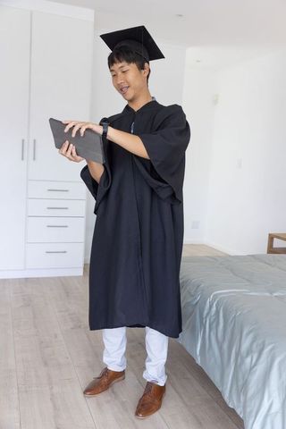 Young graduate celebrating virtual graduation using tablet in modern bedroom