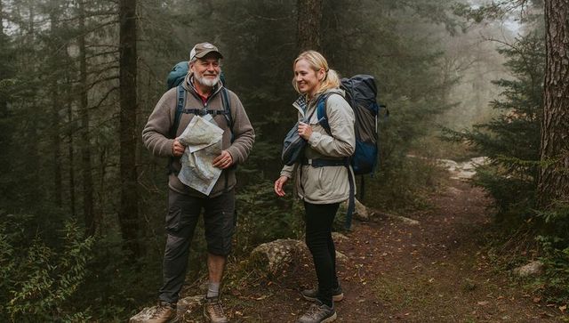 Senior man and woman hiking misty forest trail consulting map with backpacks