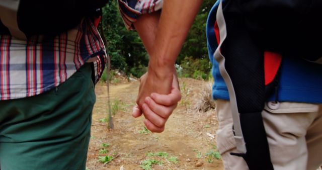 Two people are holding hands while hiking on a trail, with copy space. Their close bond is evident as they navigate the natural landscape together.