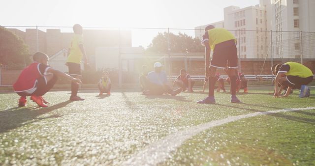 Youth soccer team warming up, stretching during sunset on urban outdoor field, emphasizing themes of sportsmanship, fitness, and teamwork in a city environment. Suitable for advertisements, sports promotions, fitness campaigns, and community outreach involving urban youth athletics.
