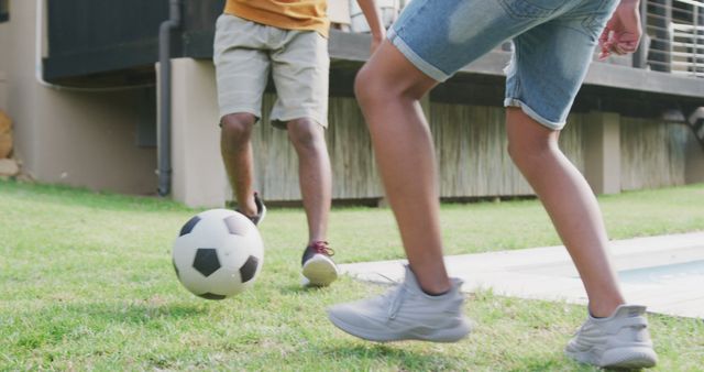 Happy diverse male teenage friends playing football in garden, slow motion. Spending quality time at home together.
