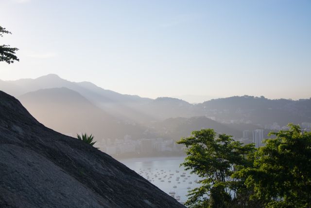 Sun streaming through mountains creates a beautiful early morning view of Rio de Janeiro Bay. With the early sunlight adding a soft glow, this image can be used in travel brochures, nature promotions, or any material highlighting the scenic beauty of Brazil.