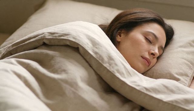Sleeping woman wrapped in beige linen duvet in calm neutral bedroom for wellness
