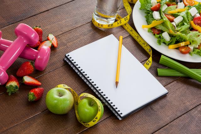 Healthy diet concept with personal organizer, fresh fruits, salad and measuring tape on table