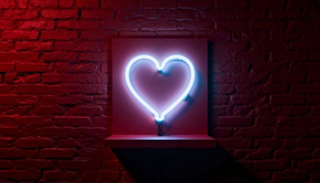 Cyan neon heart sign casting cool glow on red brick wall with minimal shelf and cable