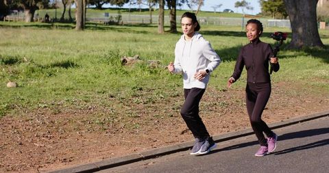 Two women jogging while filming with handheld gimbal on park path