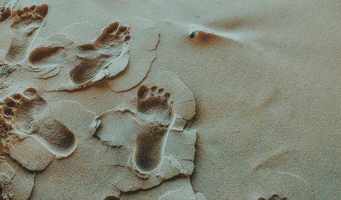 Barefoot footprints leaving trail on rippling wet sand with cracked texture and shell accent