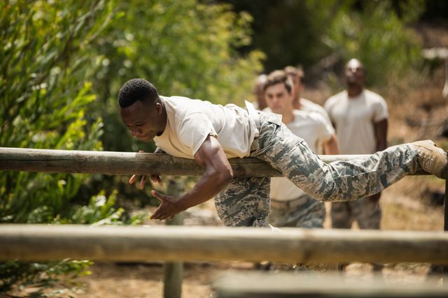 Military soldiers are training on a fitness trail at boot camp, navigating an obstacle course. This image can be used to depict themes of physical training, discipline, teamwork, and endurance in military settings. It is suitable for articles or advertisements related to military training, fitness programs, or teamwork exercises.