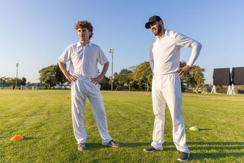 Two cricket players standing hands on hips on sunlit field during training with cones