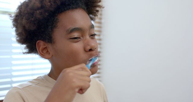 Young boy is brushing teeth, promoting good dental hygiene in a casual bathroom setting. This can be used in educational materials, health-related articles, or advertisements for dental products and personal care. It emphasizes the importance of building healthy habits from a young age.