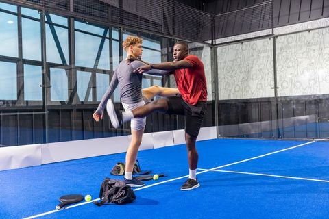 Multiethnic male athletes stretching on indoor padel court during dynamic training session