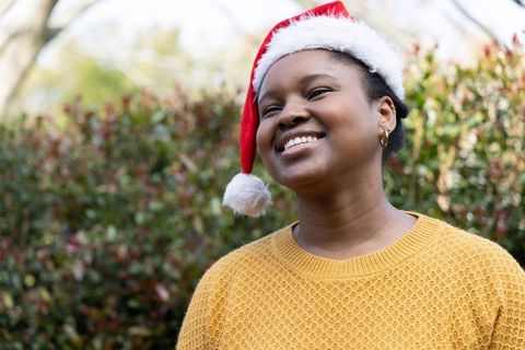 African american woman wearing santa hat and mustard sweater smiling outdoors christmas