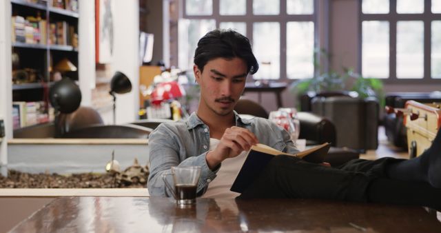 Young Man Reading Book in Cozy Modern Library with Coffee - Download Free Stock Images Pikwizard.com