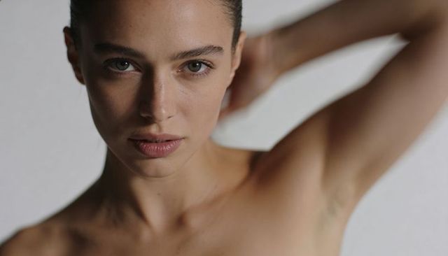 Intimate close-up of female model gazing into camera holding arm up and bare shoulders