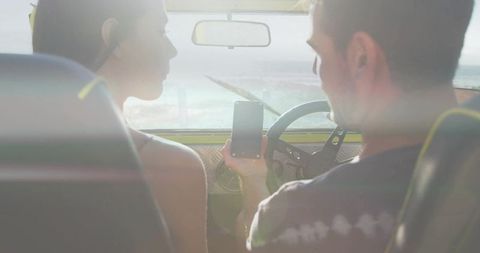 Couple Sharing Smartphone While Parked on Coastal Road, Sunlit Dashboard, Ocean View