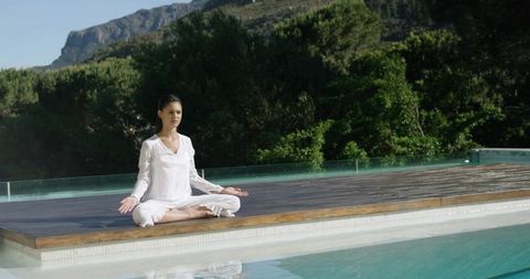Teen Meditating in Lotus on Wooden Pool Deck with Turquoise Water and Mountain View