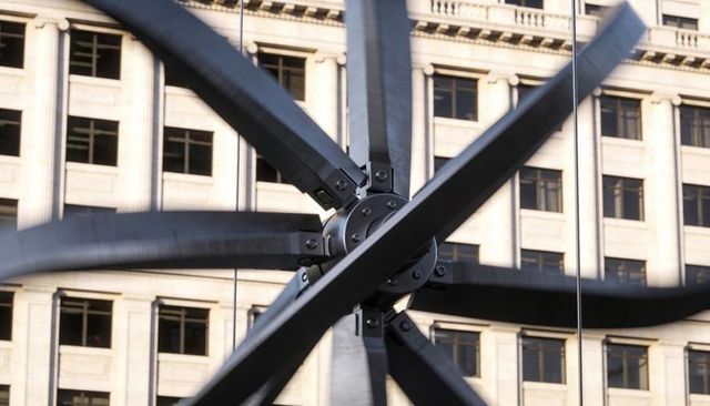 Industrial steel rotor sculpture reflecting urban office facade with radial propeller hub