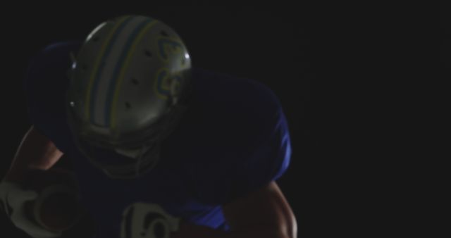 Blurred shot showing an American football player in uniform and helmet running against a dark background. This image captures intense action and could be used in sports-related marketing, advertisements, motivational content, or highlighting the thrill of American football.