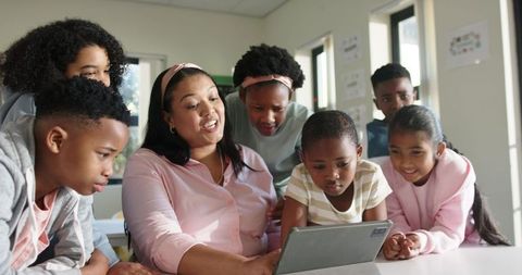 African American teacher guiding diverse students using tablet for collaborative learning
