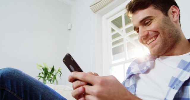 Young Man Smiling While Using Smartphone in Bright Living Room - Download Free Stock Images Pikwizard.com