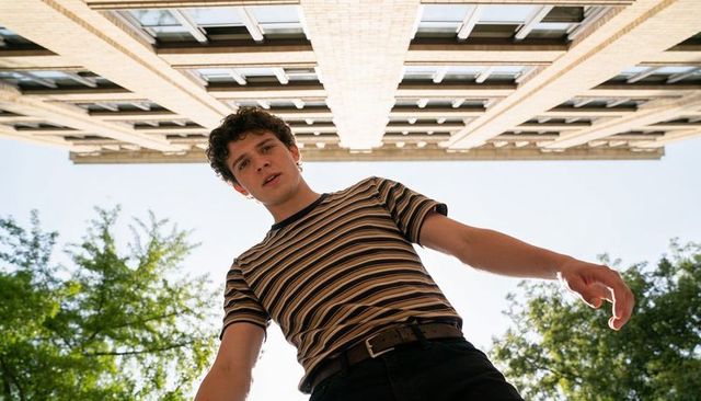 Leaning young man reaching down low-angle urban view wearing striped tee, belted jeans